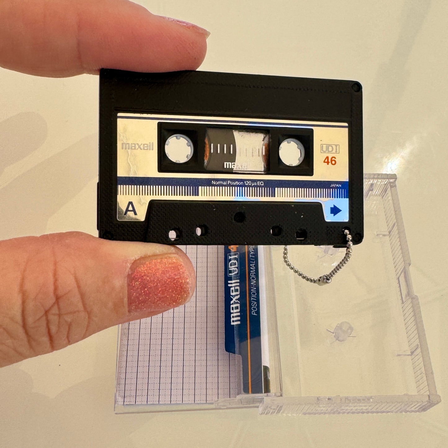 Cassette tape key chain held by a hand with a clear plastic case in the background.