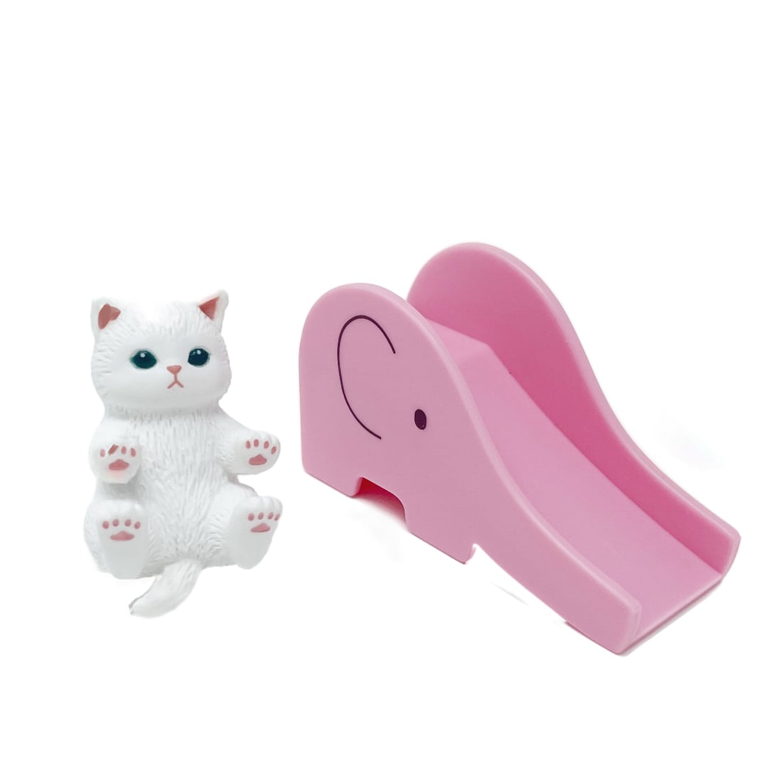 A small white toy cat figurine is next to a pink toy slide in the shape of an elephant.