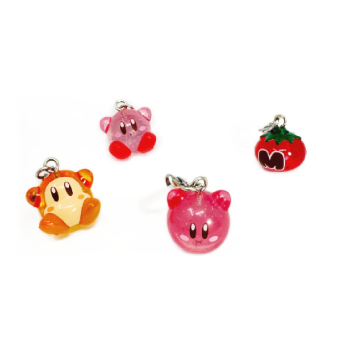Four Kirby Sparkling Charms hang from clips on a pen. they are glittery. Four Sparkling Glitter Kirby Charms. figures include Kirby, Floating Kirby, Waddle Dee, and the Maxim Tomato.