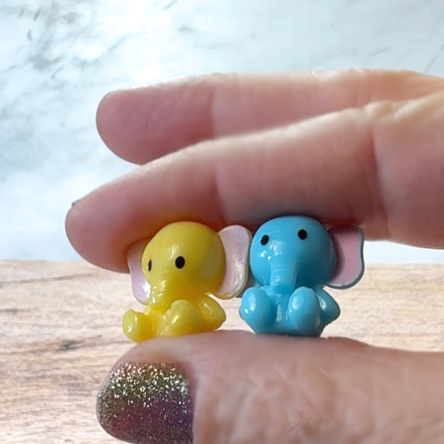 Fingers hold the teeny tiny toy elephants out of the packaging.