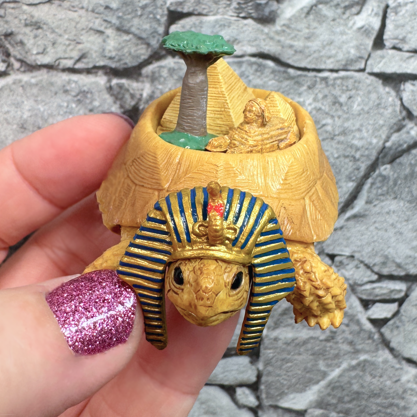 A hand holds a toy tortoise figure carrying a scene from Egypt on his back. This capsule toy series represents 6 continents.