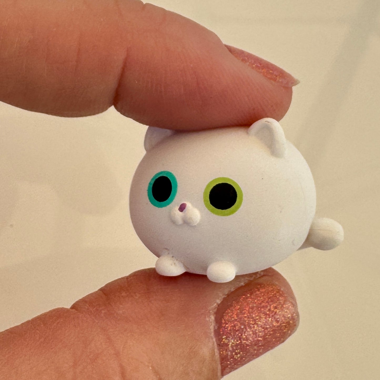 Small white cat figurine held between two fingers against a beige background
