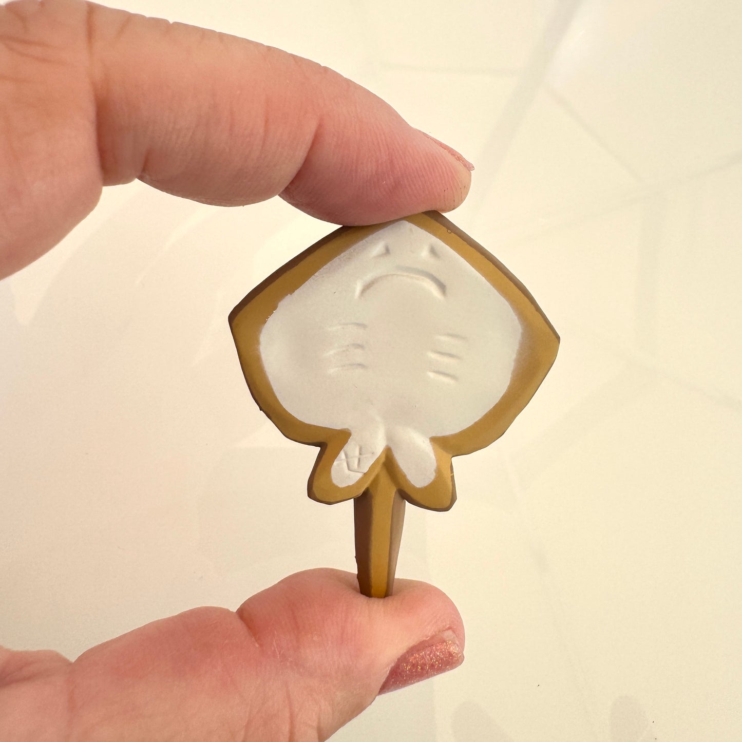 Hand holding a small decorative item with a leaf design on a plain background