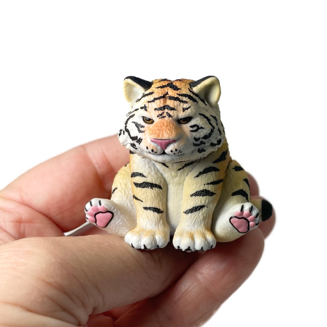 A hand holding a small Rben Studios toy tiger figurine.