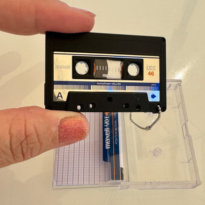 Cassette tape key chain held by a hand with a clear plastic case in the background.