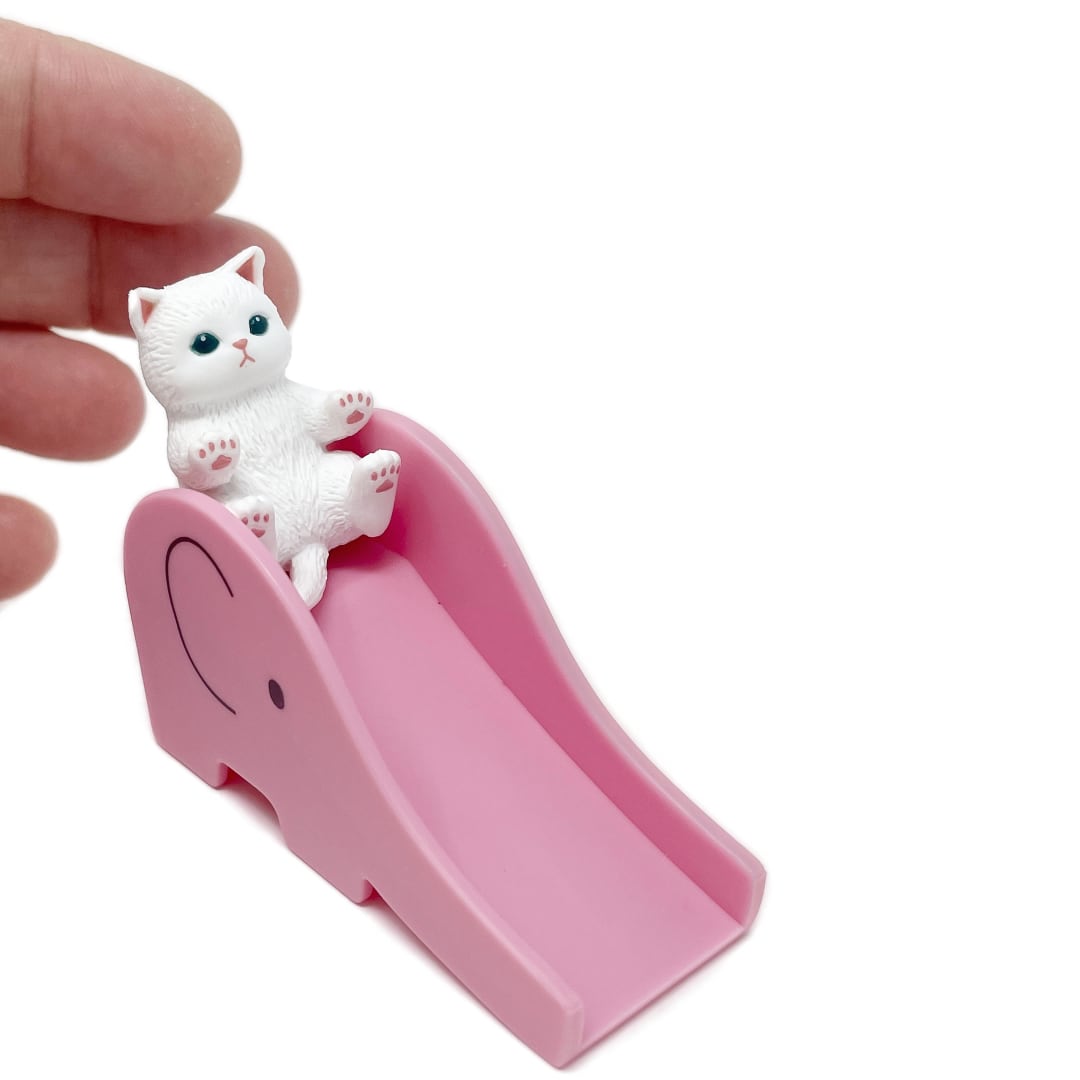 A hand is behind a tiny toy cat figurine on a pink toy elephant slide.
