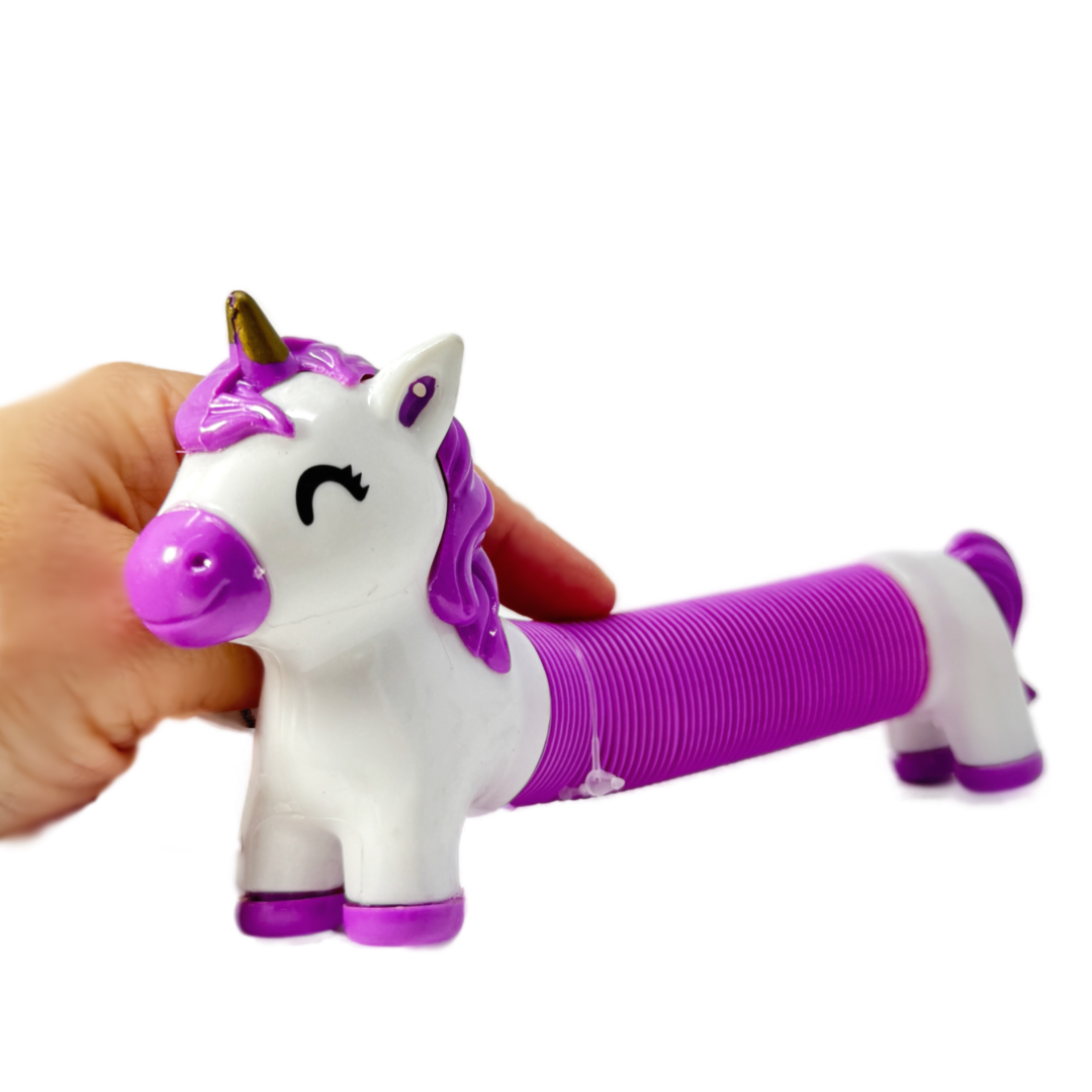 A hand holds a purple and white toy unicorn pop tube fidget.