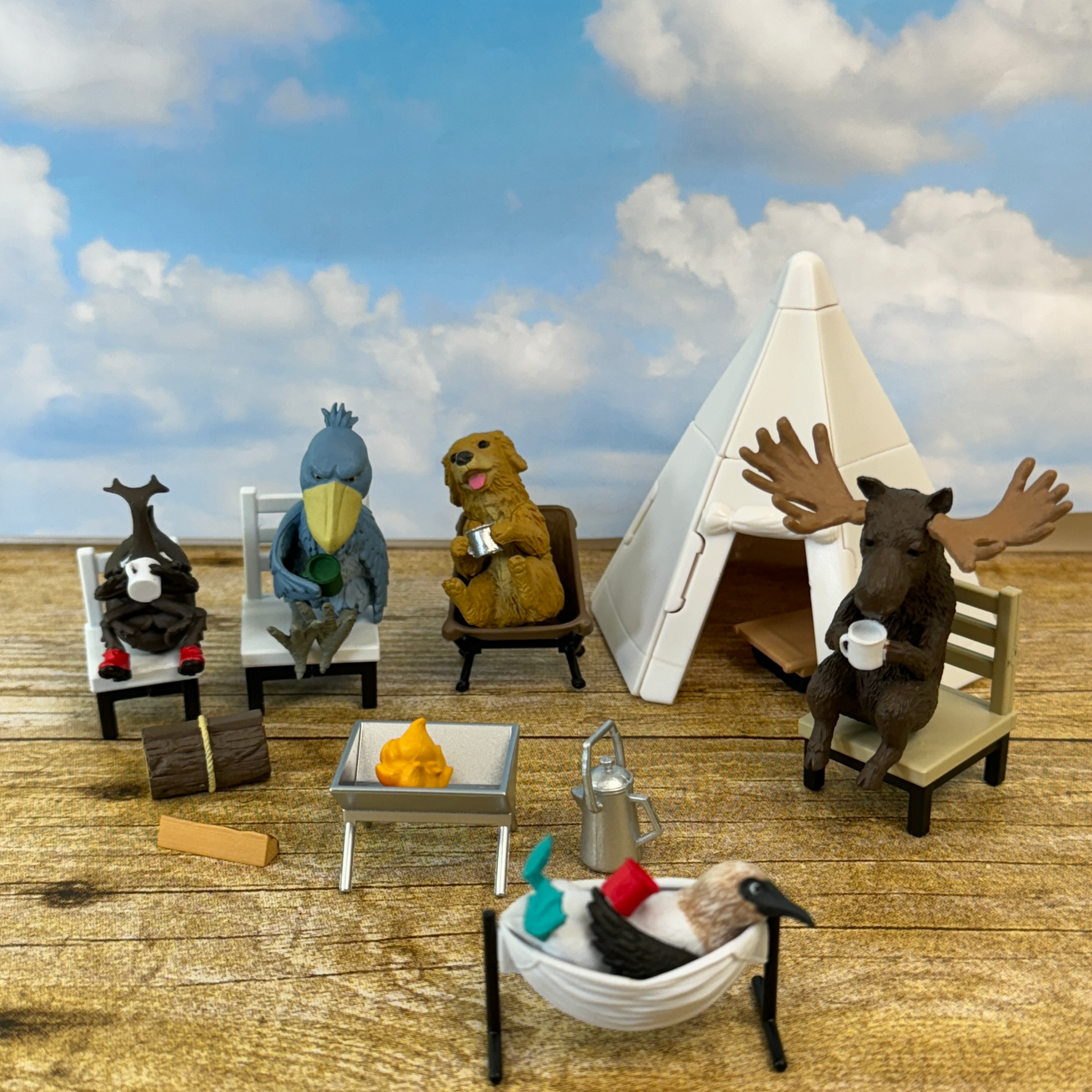 5 toy animals are sitting in camp chairs around a campfire in front of a blue sky.