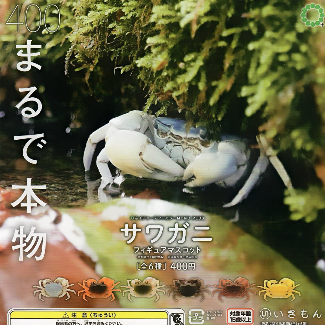 Japanese collectible crab figurine packaging or label featuring a realistic photo of a blue crab in a mossy stream, with large white Japanese text and a row of small crab color options along the bottom.