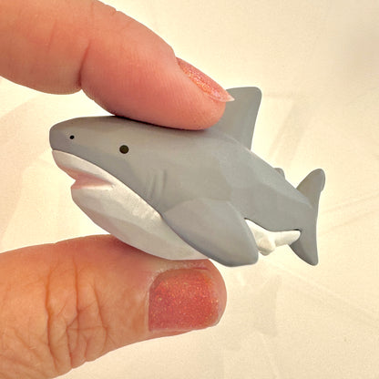 Small shark figurine held between two fingers against a plain background
