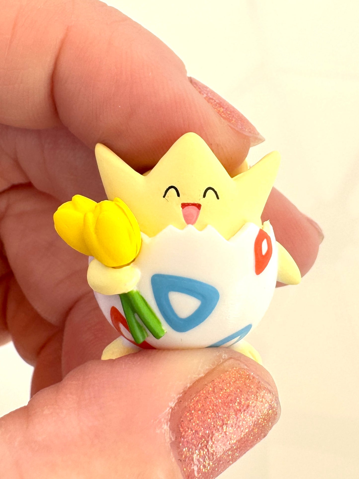 Small figurine of a Pokémon cartoon character holding flowers, held between fingers against a neutral background