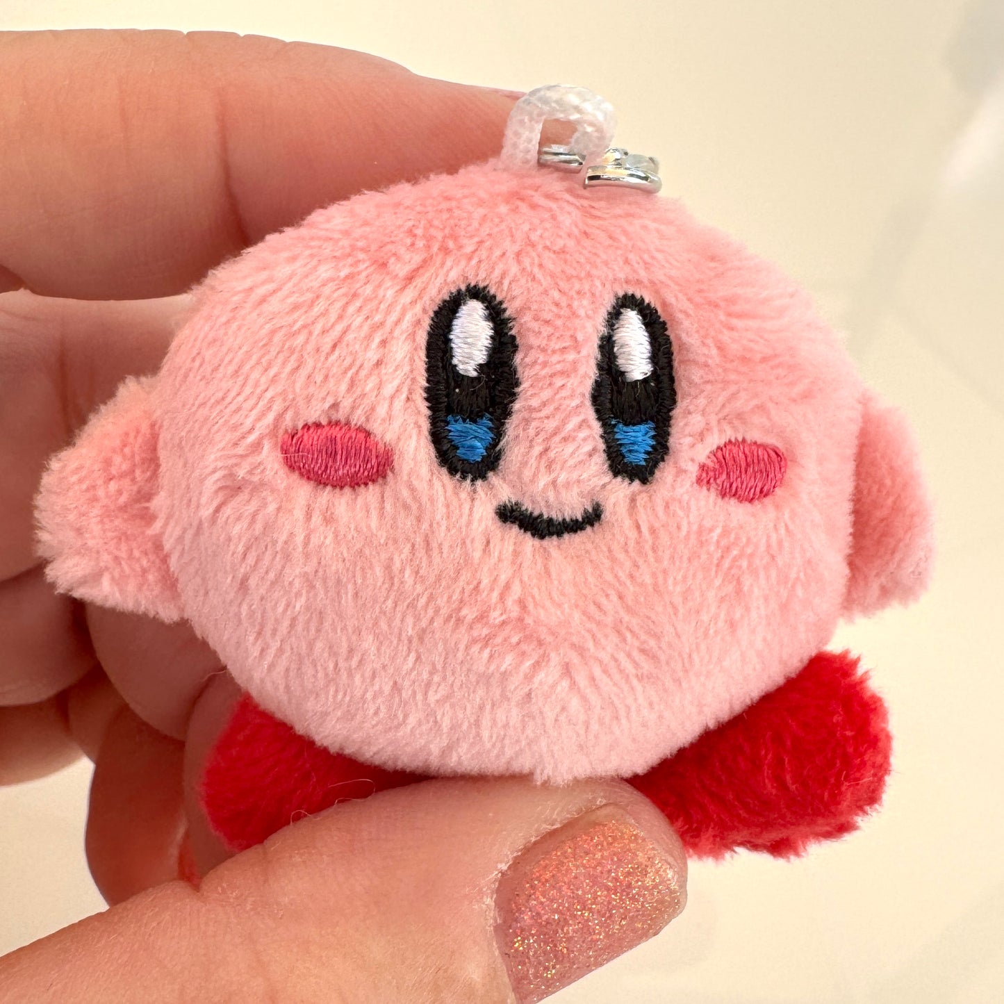 Plush keychain of a Kirby character with black eyes and red accents held in a hand.