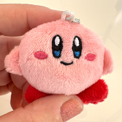Plush keychain of a Kirby character with black eyes and red accents held in a hand.