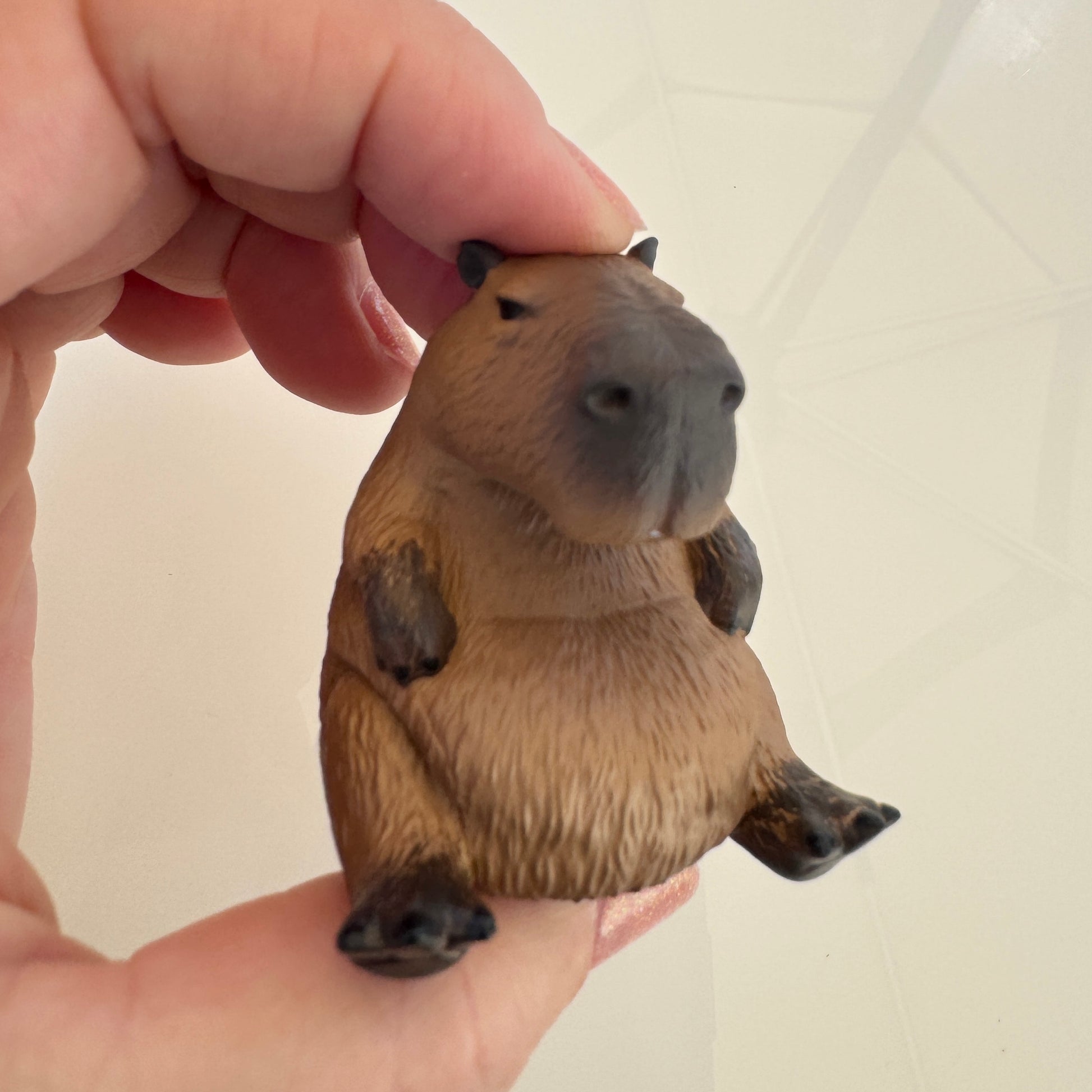 Hand holding a small capybara figurine against a plain background