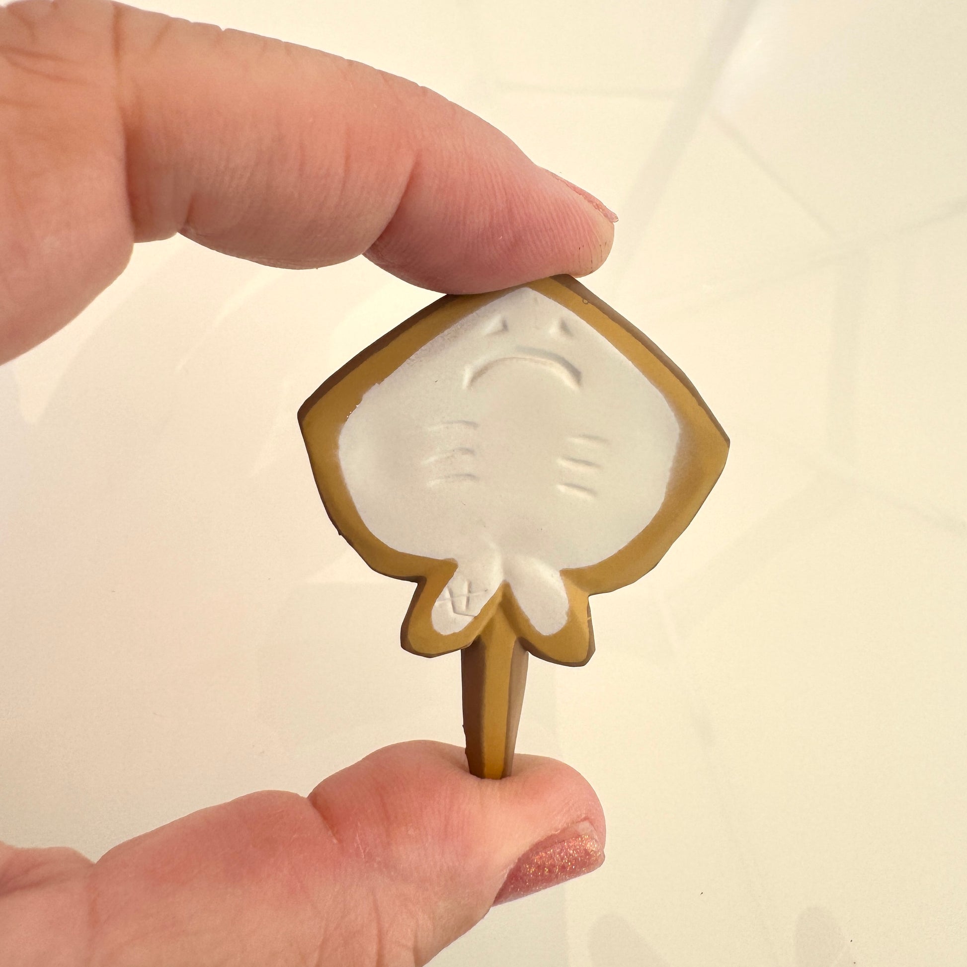 Hand holding a small decorative item with a leaf design on a plain background