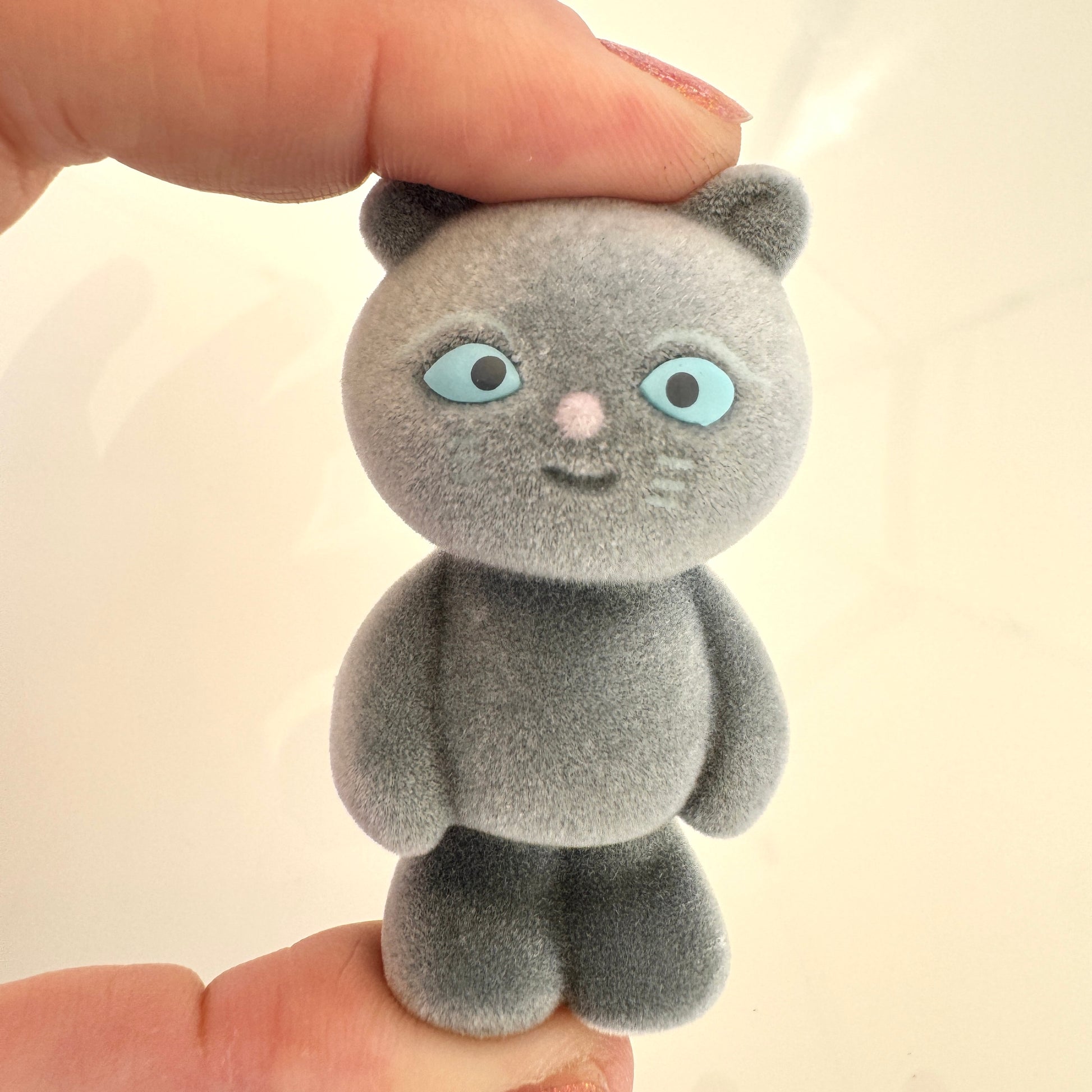 Small gray plush cat toy held between two fingers against a light background