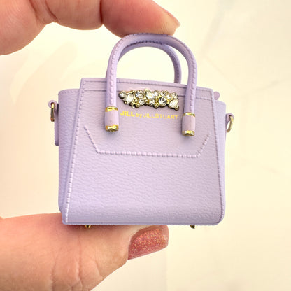 Small purple handbag with decorative clasp held by a hand against a beige background
