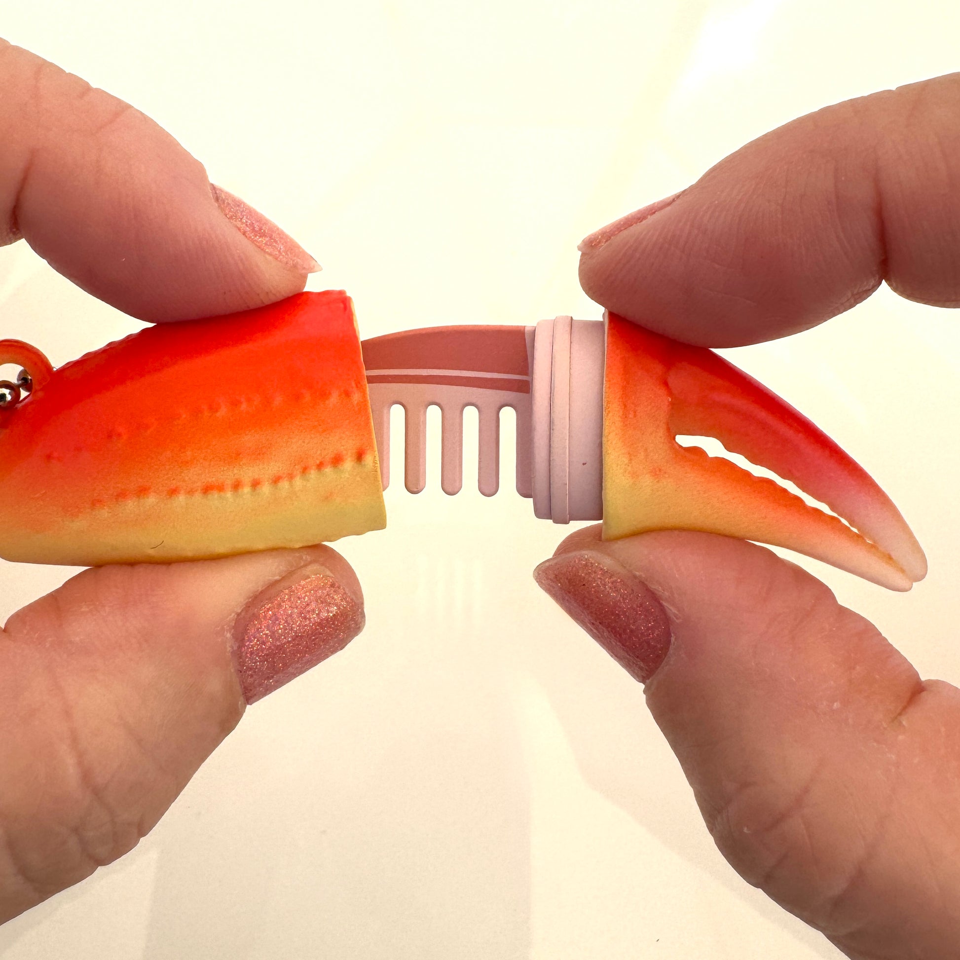 Person holding a crab claw-shaped hair comb on a beige background
