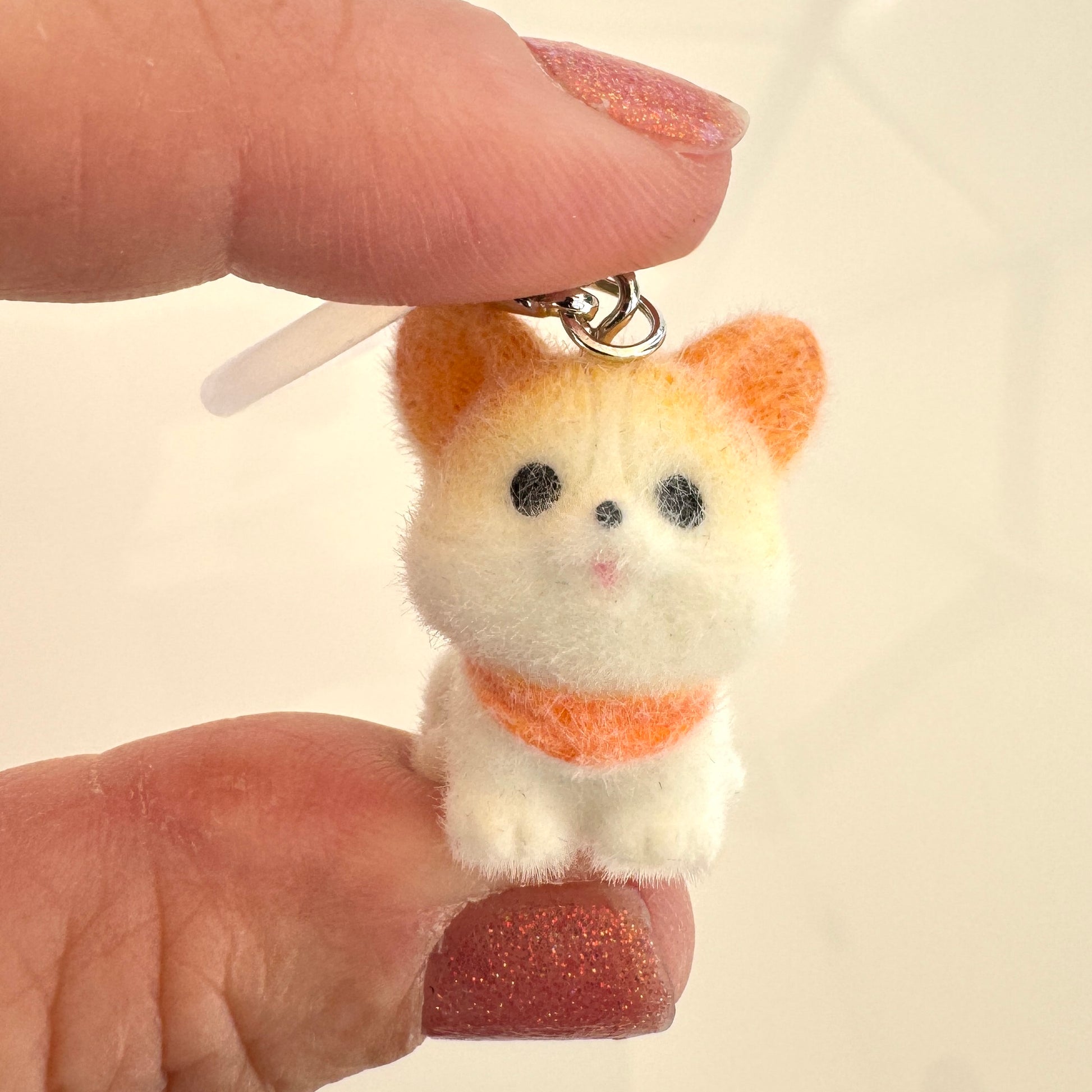 A hand holds a tiny fluffy dog figurine with a charm clasp