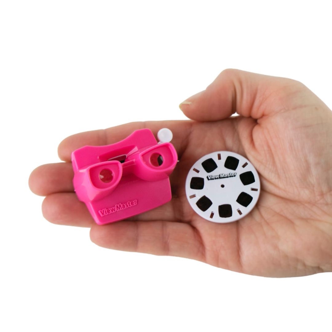 A hand holds a mini pink ViewMaster and an image disk.