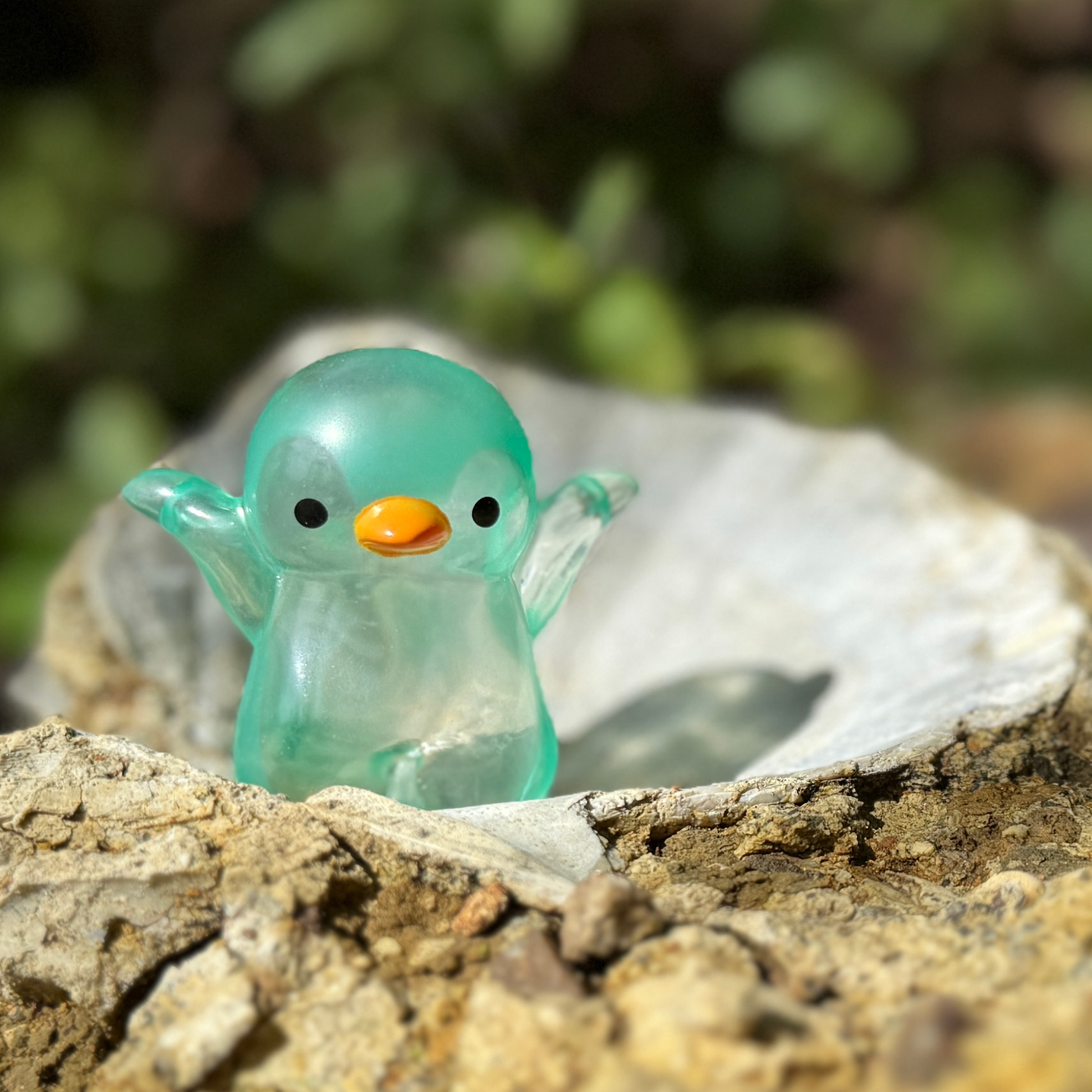 A green penguin squishy toy resting in a shell fossil in nature