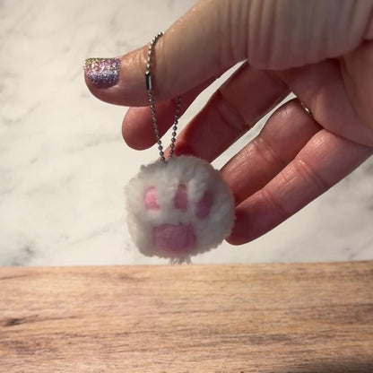 A cat paw pom pom handmade out of yarn on a keychain