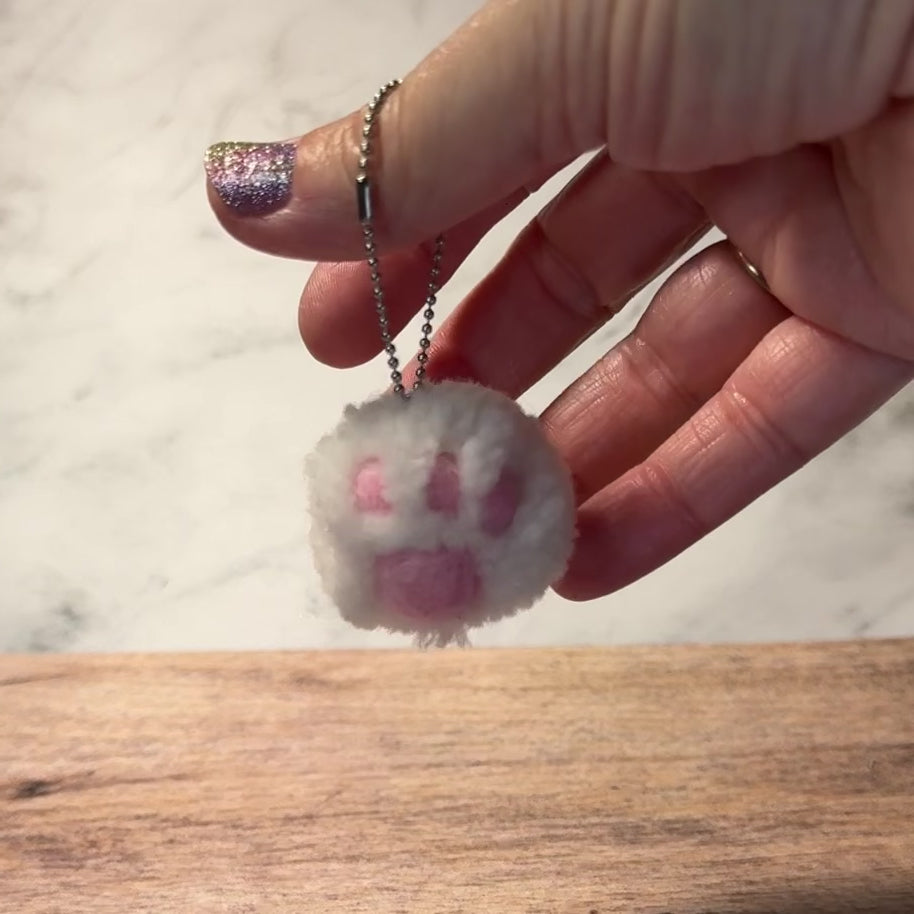 A cat paw pom pom handmade out of yarn on a keychain